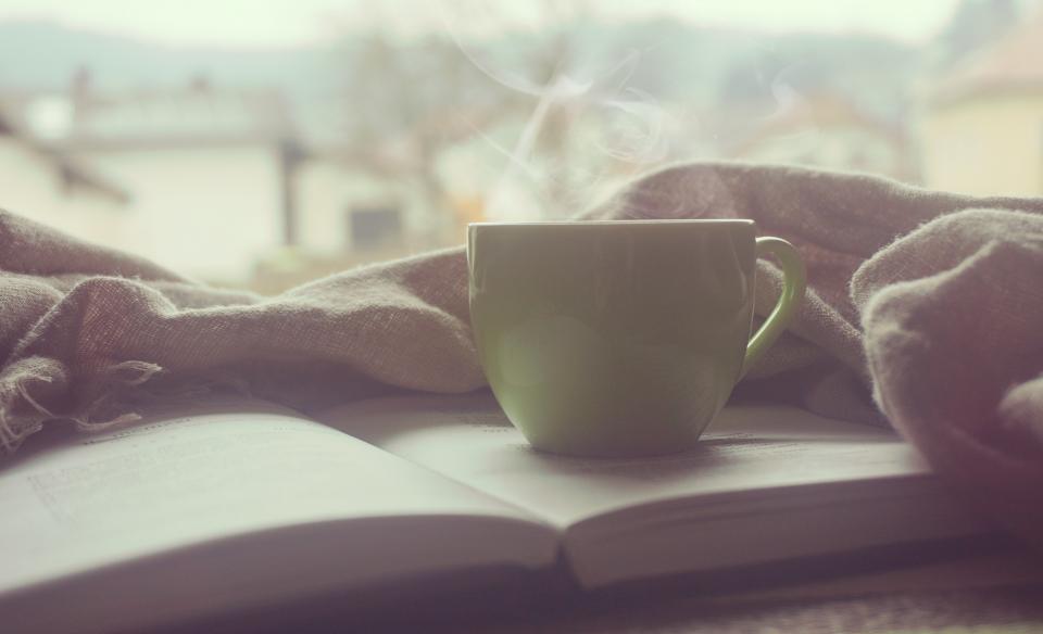 A steaming cup of coffee resting on an open book with a linen blanket - the reading ritual